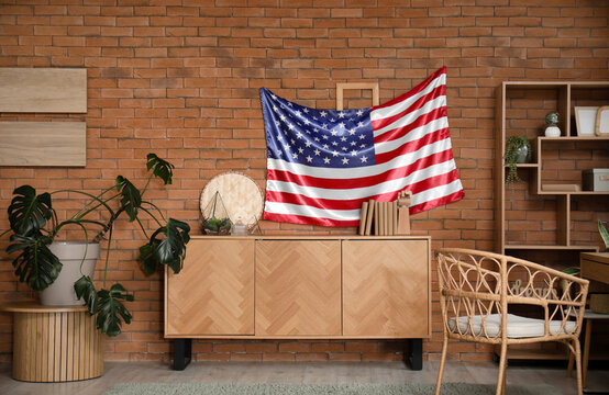 Stylish room with chest of drawers and USA flag on brown brick wall