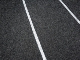 Wall Mural - Track and Field Running Lanes. Overhead view of a rubber black running track surface with white lane lines. Surface level view of the textured artificial black surface. There is a slight curve. 