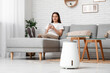 © Pixel-Shot - Young woman using mobile phone on comfortable sofa near modern humidifier in stylish living room