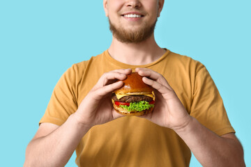 Wall Mural - Young man with tasty burger on blue background