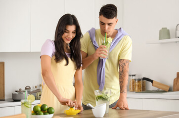 Canvas Print - Happy young couple squeezing lime juice for mojito in kitchen