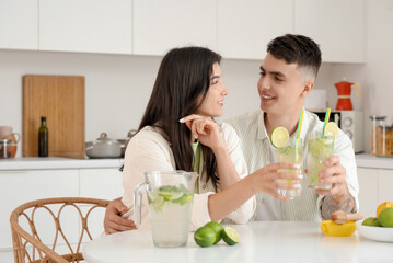 Canvas Print - Happy young couple with glasses of mojito and ingredients sitting in kitchen