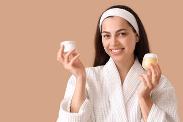 Sticker - Beautiful young happy woman in bathrobe with jars of cream on beige background