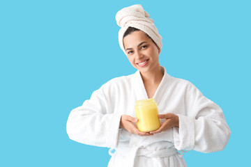 Wall Mural - Beautiful young happy woman in bathrobe with jar of cosmetic product on blue background