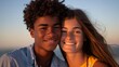 © Irina Kozel - A young black man with short curly hair and a cheerful white woman with brown hair hugging each other on the beach at sunset, she is wearing a yellow dress, he is in a blue shirt
