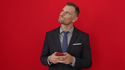 Poster - Smart young hispanic man in suit smiling, looking away and thinking while using smartphone over isolated red background