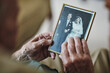 © NonVig/peopleimages.com - Senior man, hands and vintage photo for memory in home, retirement and nostalgia for mourning. Male person, picture and remember in living room, history and grief on past life or retro wedding image