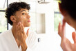 © WavebreakMediaMicro - Applying skincare cream, teenage boy in white robe looking in mirror