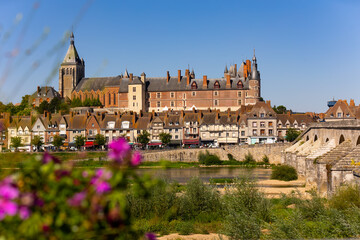 View of Gien cityscape on bank of Loire with row of townhouses along embankment, medieval renaissance castle and arched bridge across river on summer day, Loiret, France