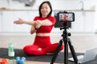 © sofiko14 - Woman instructing online yoga class stretching arms on a yoga mat. Filming with smartphone in modern bright kitchen. Concept of fitness, online teaching, and healthy lifestyle.