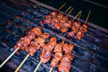 Satay is being grilled on a grill using coals and emitting smoke