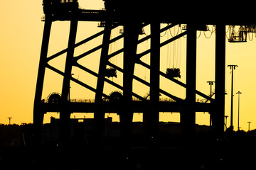 Wall Mural - Sunset silhouette of container ship loading cranes.