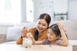 © David - Setting good example. Young parent mother teach child little daughter girl to manage finances save money spend earnings with economy plan family budget. Friendly mom and kid thrift coins in piggybank