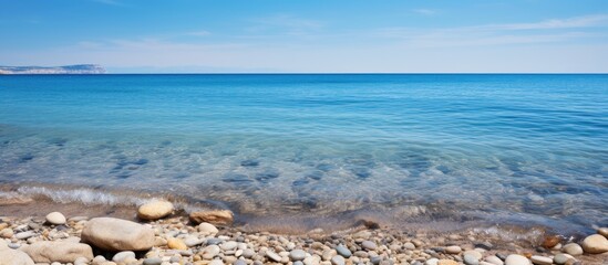 Wall Mural - Copy space image showcasing rocks and sand in the ocean under a clear blue sky with a water backdrop.