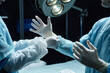 © Seventyfour - Side view of unrecognizable surgeon putting on gloves in operating room with medical assistant helping copy space