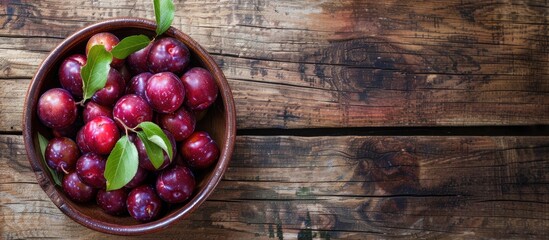 Poster - Juicy organic plums in a rustic ceramic bowl on a wooden background, creating a charming copy space image in a top view.