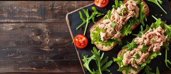 Poster - Top-view image of canned tuna toasts or sandwiches with lettuce and arugula on a dark wooden backdrop, offering ample copy space.
