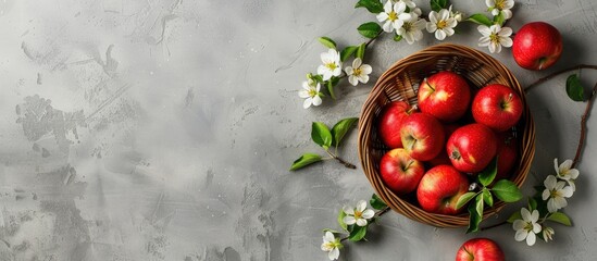 Poster - A flat lay view of a basket with ripe red apples, apple blossom flowers, and copy space image from above.