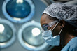 © Seventyfour - Side view portrait of female surgeon under surgical lights in operating theater copy space