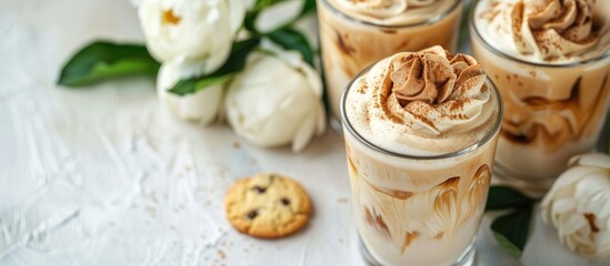 Leinwandbilder - Korean trend, Dalgona Coffee with milk and ice, a cold drink with whipped brown cream in a glass on a white table with cookies and peonies, in a top view copy space image.