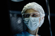 © Seventyfour - Dramatic closeup portrait of senior woman as female surgeon wearing mask in operating room lit by blue light copy space