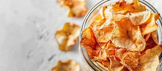 Close-up of organic apple chips in a glass jar on a white background with space for text, featuring a homemade crispy appearance and sun-dried texture. Copy space image