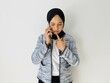 © Siti Fatonah - Young Asian woman using mobile phone having doubts while looking down. Female wearing wearing black hijab and tweed blazer isolated on white background.