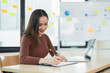 © Natee Meepian - Young Professional Woman Working at Desk with Laptop and Documents in Modern Office Environment