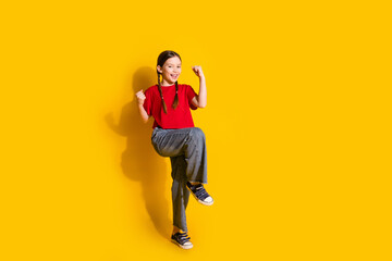 Poster - Full size photo of lovely small girl raise fists empty space wear t-shirt isolated on yellow color background