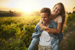 © Stratford/peopleimages.com - Happy couple, nature and piggyback in sunset for adventure, tourism and holiday together with romance. Excited young people walking with support, love and fun in meadow or countryside for vacation
