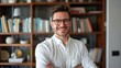 © liliyabatyrova - A close-up portrait of a man in a white shirt, smiling confidently with his arms crossed, standing in front of a bookshelf filled with books