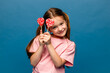 © Irina Mikhailichenko - Happiness, childhood, kid and sweets. A happy little girl holding a heart shaped lollipop caramel on a stick, A festive candy in the hands of child in pink t-shirt on blue background. Valentines Day