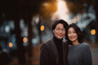 © NaphakStudio - Middle-aged couple smiling warmly, posing together outdoors at dusk with soft bokeh lights in the background.