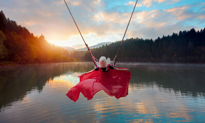 Wall Mural - Beautiful blonde woman in a long red dress is swinging on a swing - Morning evaporation of water over the lake-Autumn landscape with Karagol(Black lake) - popular destination Black Sea, Savsat, Artvin