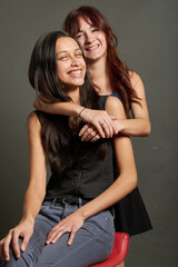 Two teenage friends sitting together on a red stool. They are hugging each other, dressed in casual, teenage fashion. Concept of friendship, they are smiling and enjoying each other's company.