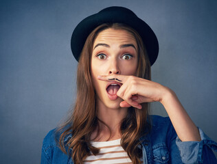 Canvas Print - Girl, finger and mustache in studio with portrait for quirky behavior, facial expression and funny face with hat. Wow, silly and hand gesture for creative humor, goofy and playful on dark background.