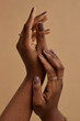 © Seventyfour - Vertical close up on female hands with soft touch gesture presenting perfect nude manicure. African American womans hands with healthy skin on beige background, skincare concept