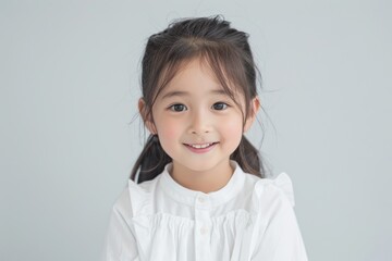 A happy little Asian girl dressed in a white t-shirt, smiling warmly at the camera. Her clean and simple look, combined with her joyful demeanor, makes this photo ideal for advertisements,