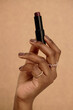 © Seventyfour - Vertical close up on Black woman hand holding cherry lipstick with dark brown manicure