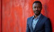 © Sang - Confident African businessman, exuding professionalism and charisma, stands against a vibrant red backdrop, dressed in a sharp navy suit.