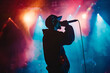 © Cadengo - The silhouette of a rapper, donning a cap and holding a microphone, delivers powerful lyrics under vibrant stage lights
