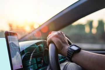 Close-up of a driver's hand on the steering wheel, with futuristic digital dashboard and navigation display at sunset.