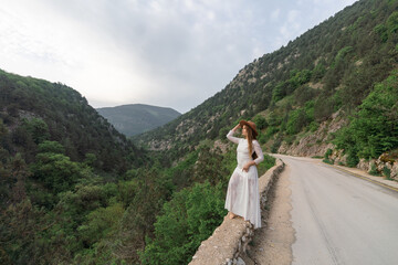 Wall Mural - A woman in a white dress stands on a road overlooking a mountain range