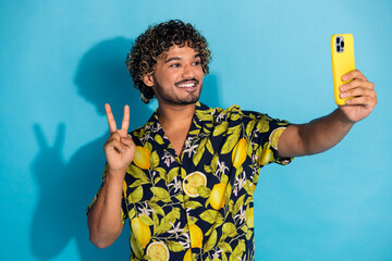 Canvas Print - Photo of nice guy with wavy hairstyle dressed print shirt hold smartphone make selfie show v-sign isolated on blue color background