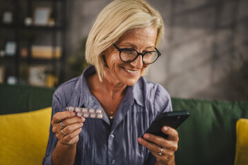 Mature woman hold the medicine and read instructions on mobile phone