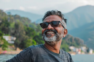 Wall Mural - Portrait of a smiling indian man in his 40s wearing a trendy sunglasses while standing against serene lakeside view
