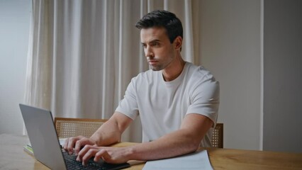 Wall Mural - Serious man working remotely on laptop at home desk. Smart businessman typing 