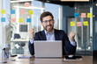 © Liubomir - Happy businessman wearing suit celebrating success at office desk with laptop. Concept of achievement, motivation, business success. Office setting with sticky notes on glass wall in background.
