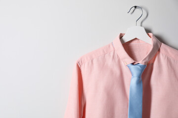 Wall Mural - Hanger with shirt and necktie on light wall, space for text