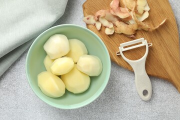 Wall Mural - Fresh raw potatoes in bowl, peeler and peels on light grey table, top view